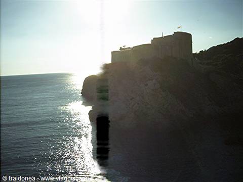 Stone fortress on rocky cliff above the sea, backlit sunlight