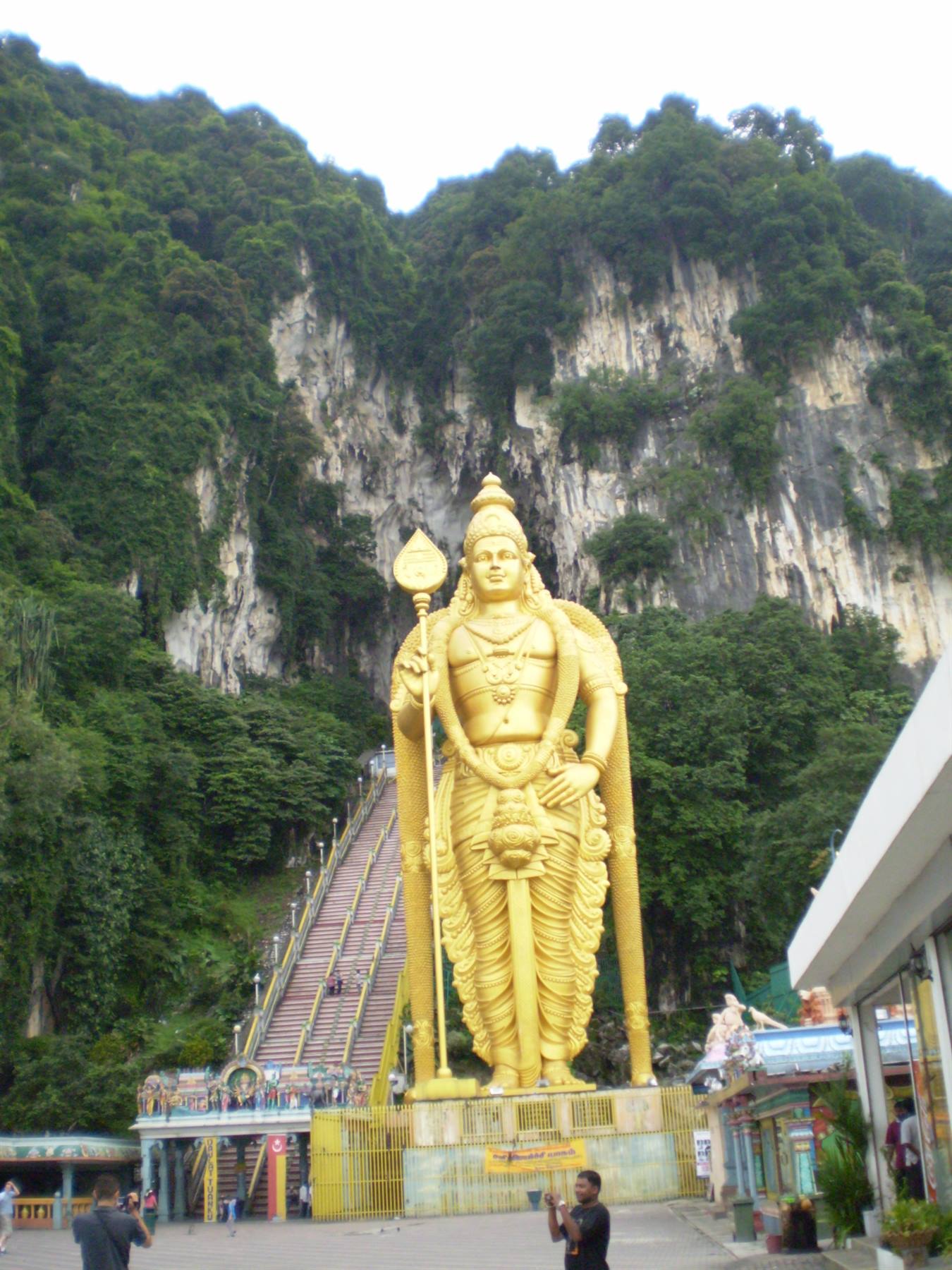 Golden Murugan statue at Batu Caves, tourists photographing below the staircase