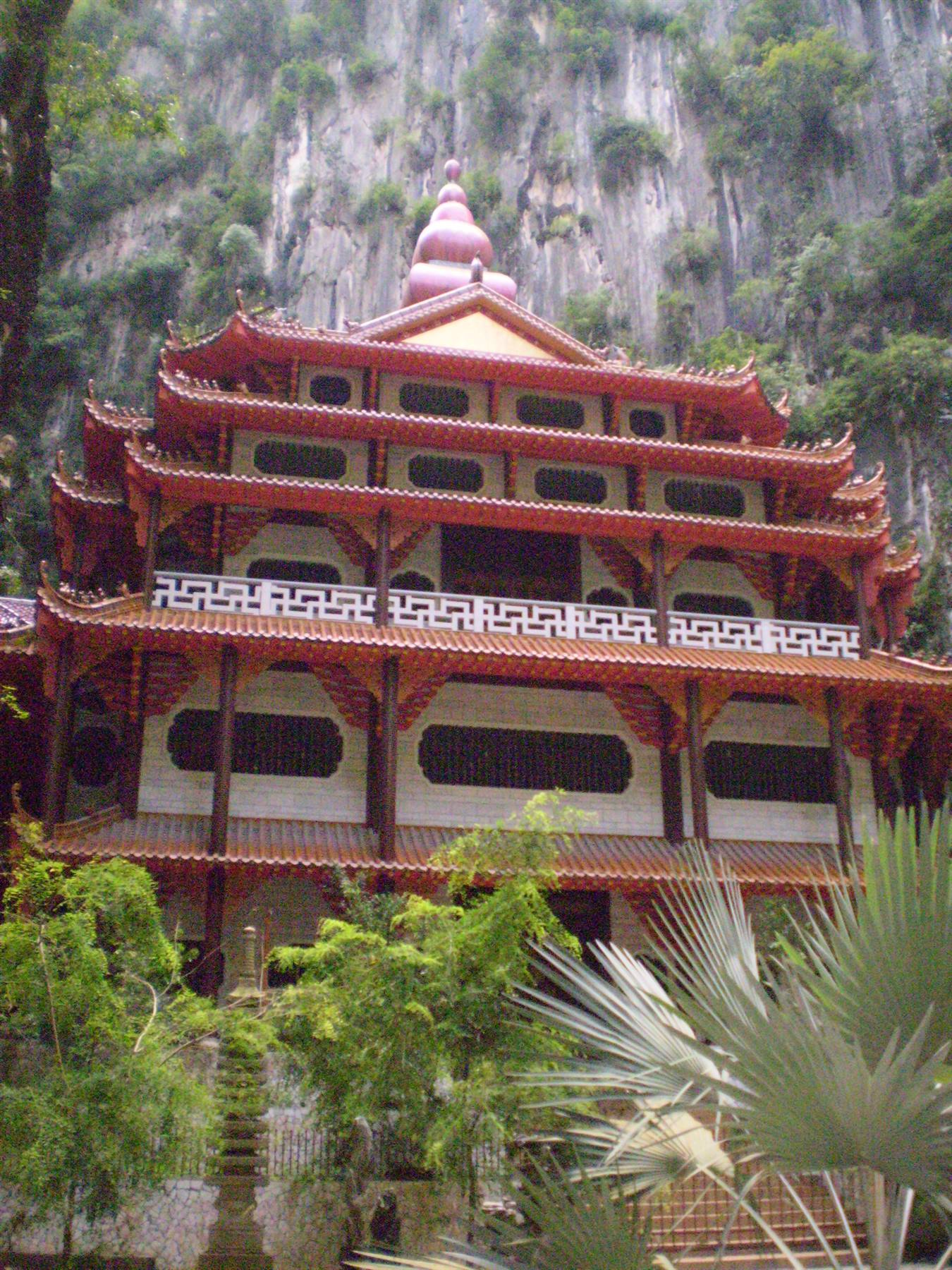 Red multi-tiered Chinese temple beneath a limestone cliff, Ipoh