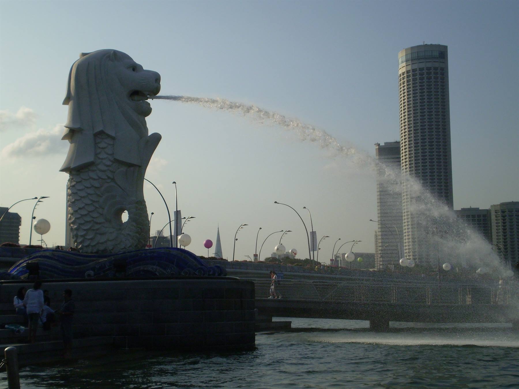 Merlion statue spouting water into the bay, skyscrapers along the waterfront