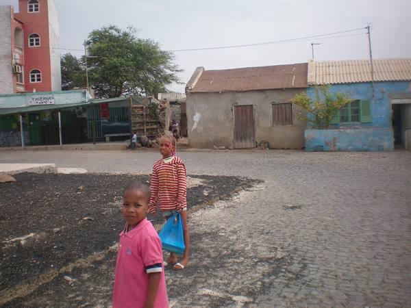 Children on a cobblestone street among colorful houses, one carrying blue bag