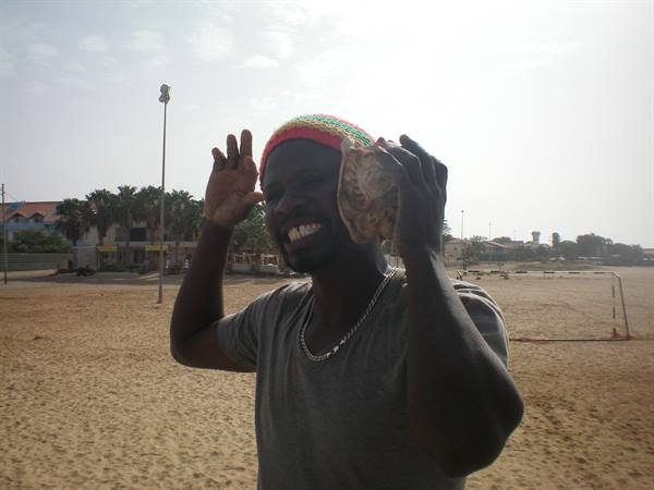 Smiling man in colorful hat holding seashell to his ear on the beach