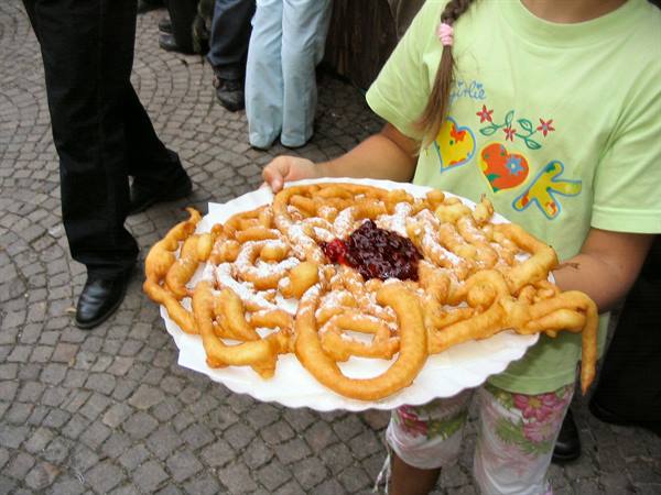 Girl in green shirt offering a big fried chiffel pastry with jam