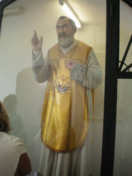 Statue of Padre Pio in golden vestments behind glass