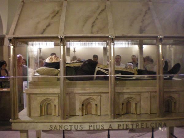 Glass tomb of Padre Pio in San Giovanni Rotondo crypt, visitors praying nearby