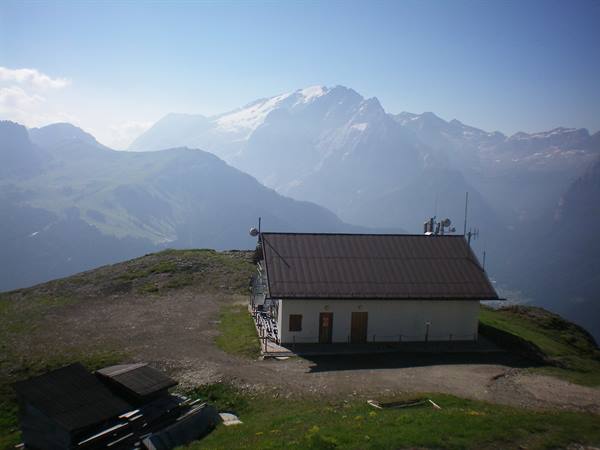 mountain hut with metal roof on alpine meadow, snowy Marmolada behind