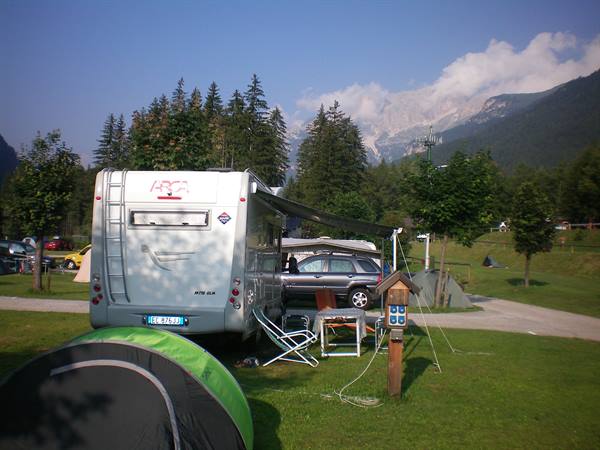 Camper van and green tent on campsite meadow among firs and Dolomites