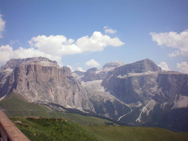 Gardena Pass, Dolomites: rocky walls above green meadows, wooden railing in foreground
