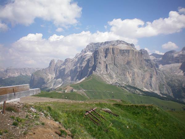 Dolomite massif above green meadows, wooden guardrail by the road, cloudy sky