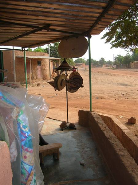 Straw hats hanging on a display stand under a corrugated metal shelter by a dirt road