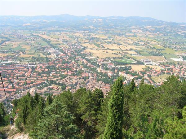 Red-roofed town among farmland and hills, seen from a wooded hillside