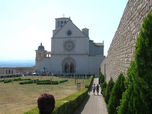 Tourists walk toward the Basilica of San Francesco in Assisi among walls and gardens