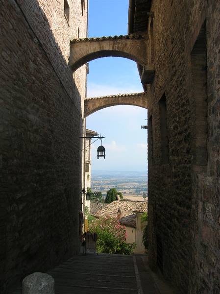 Stone arches between medieval houses in Assisi, sunlit Umbrian valley below