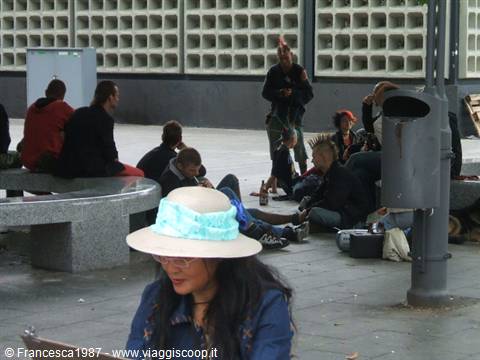 Punk youths sitting on concrete benches, woman in blue hat in foreground