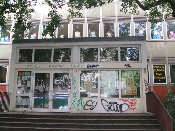 Entrance with glass windows covered in graffiti, colorful paper figures, concrete steps