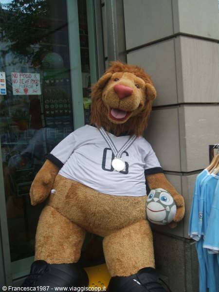 Plush lion mascot in white jersey with medal and ball outside a shop