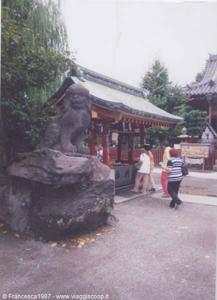 Stone lion statue in front of a red Japanese temple pavilion, visitors nearby