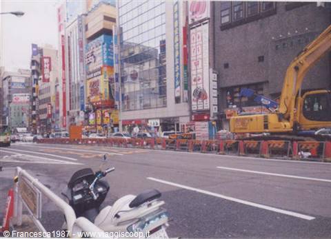 Scooter and yellow excavator at a roadworks site among Akihabara's buildings