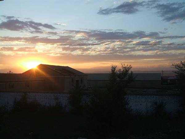 Sun rising behind house rooftops, dark trees and power lines