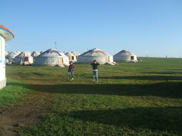 Tourists pose on the grass in front of white yurts, blue sky