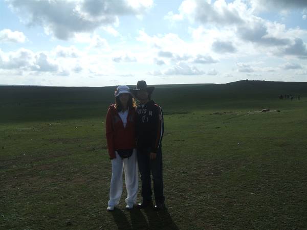 Couple wearing hats poses on green grassland under cloudy sky