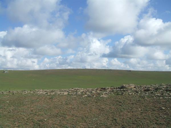 Green grassy hill under white clouds, stone piles in the foreground
