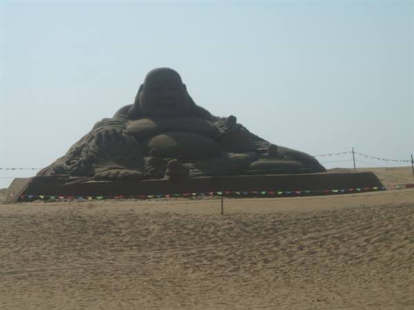 Large sand sculpture of a smiling Buddha on a sandy beach