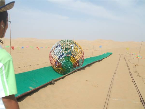 Colorful metal sphere rolling on green track between sand dunes