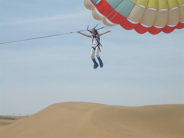 Woman with open arms parasailing above the sand dunes