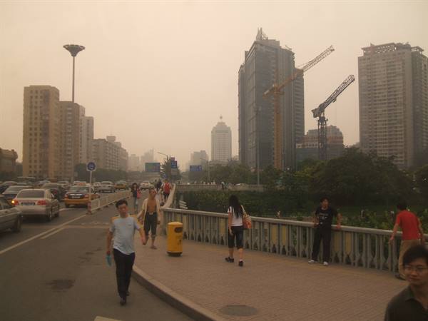 Pedestrians on a city bridge under hazy sky, skyscrapers under construction with cranes