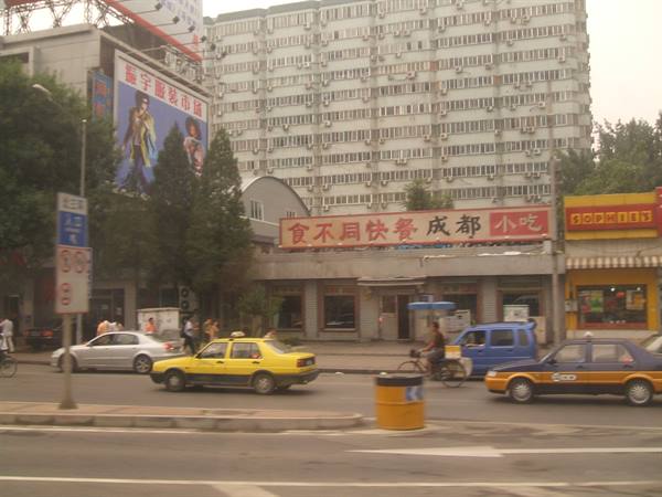 Yellow taxis and bicycles cross an intersection under Chinese shop signs