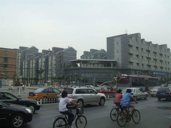 Cyclists and cars cross a busy avenue lined with grey apartment blocks