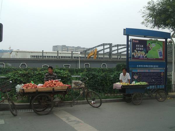 Vendors on three-wheeled carts selling peaches and bananas along the street