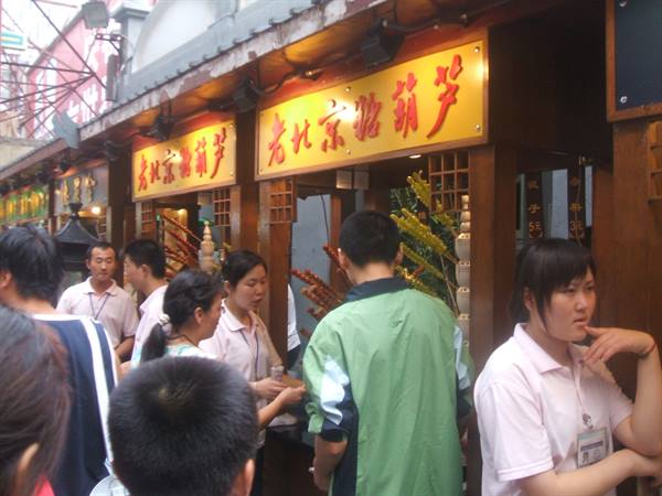 Tanghulu stalls with red and gold signs, vendors and crowds buying snacks