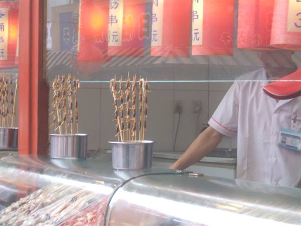 Skewer stand with metal pots under red lanterns, vendor in white uniform