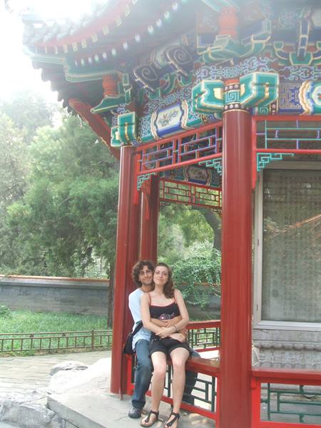 Couple sitting in a red painted pavilion, carved columns, green garden