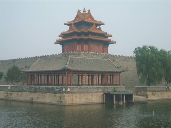 Forbidden City corner tower with golden roofs above the moat and willow
