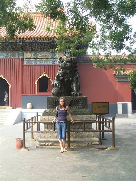 Woman beside a bronze lion in front of a temple with red walls