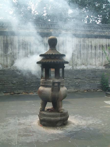 Smoking stone incense burner in a temple courtyard, old brick wall behind