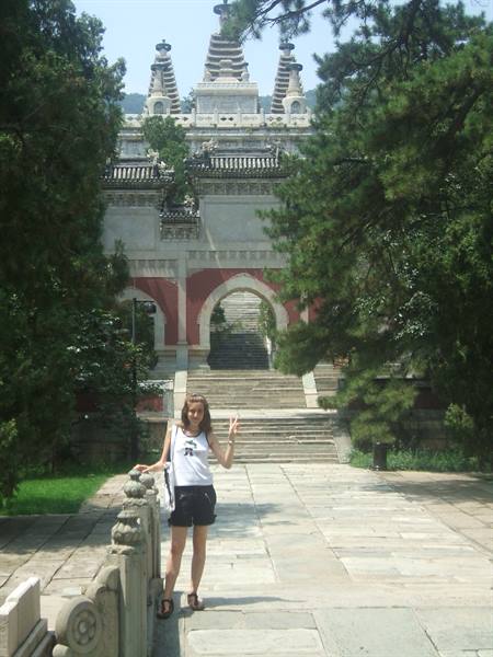 Tourist by a stone balustrade in front of a Chinese temple with twin pagodas among pines