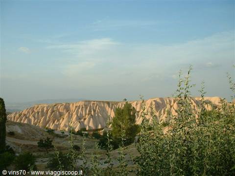 Pink rock formations of Göreme among green shrubs and trees, blue sky