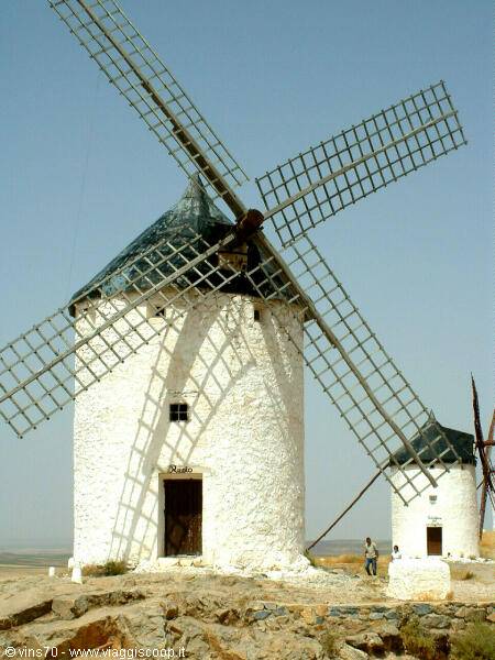 White windmills of Consuegra, wooden blades on rocky hill, tourists nearby