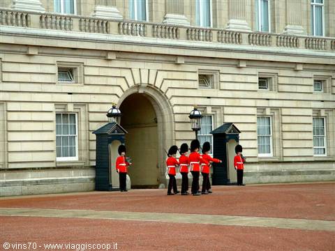 Red-coated guards in bearskin caps march in front of Buckingham Palace, London