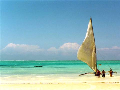 Fishermen beside a white-sailed dhow on sandy beach, turquoise water