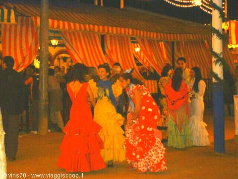 Women in flamenco dresses dance under striped tents at Seville's Feria de Abril