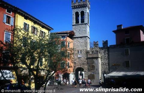 Stone Apponale Tower in Riva del Garda, tourists in the square under blue sky
