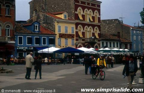 People and a cyclist in a square with colorful buildings and white kiosks