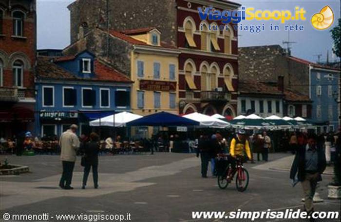 People and a cyclist in a square with colorful buildings and white kiosks