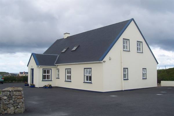 White house with grey slate roof under cloudy sky, stone wall nearby