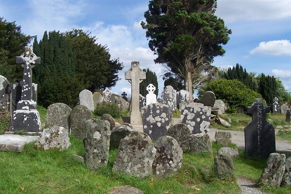 Ancient graveyard with Celtic crosses and lichen-covered stone graves beneath blue sky